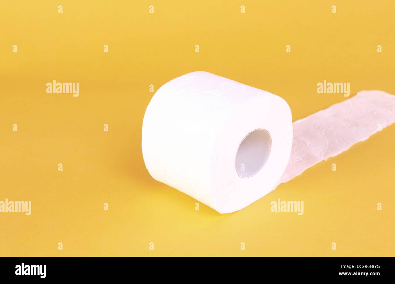 A single roll of white toilet paper lying horizontally on a bright yellow background Stock Photo