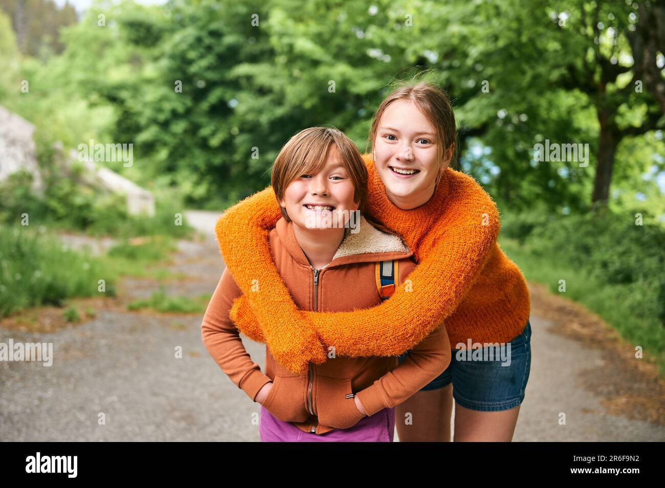 Outdoor portrait of two funny kids hugging each other, teenage sister and little brother spending time together outside Stock Photo