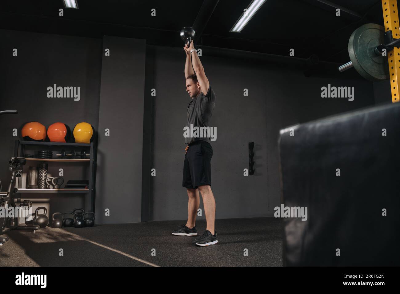 Handsome athletic young man lifting kettlebell with two hands crossfit workout. Muscular man holding kettlebell overhead at gym Stock Photo - Alamy