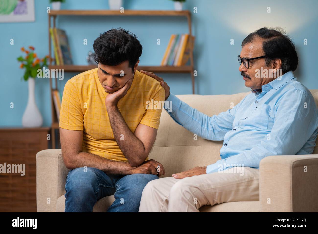 Indian senior father consoling by giving confidence to adult son at home - concept of depression, emotional comfort and caring parenthood. Stock Photo