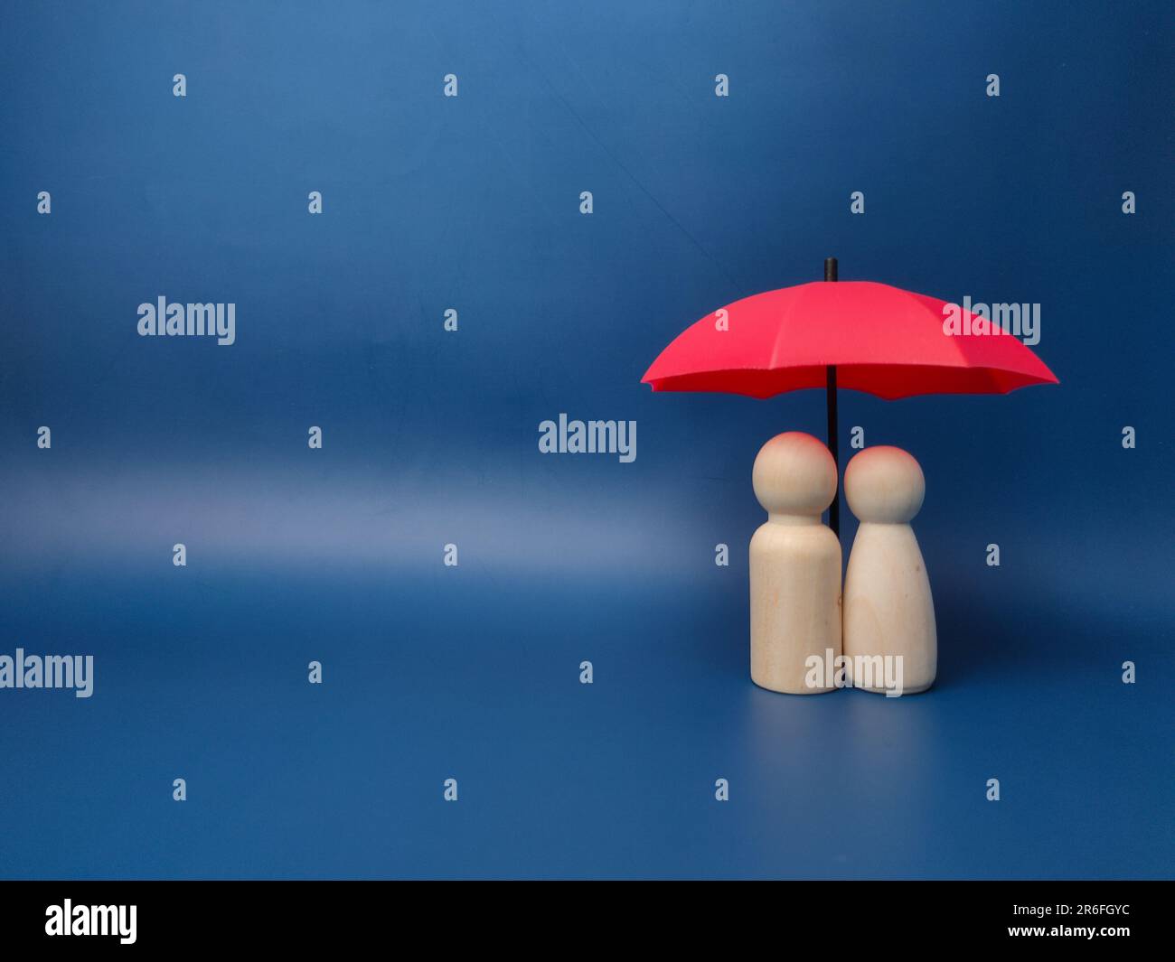 Two figures standing beneath a red umbrella on a blue background Stock Photo