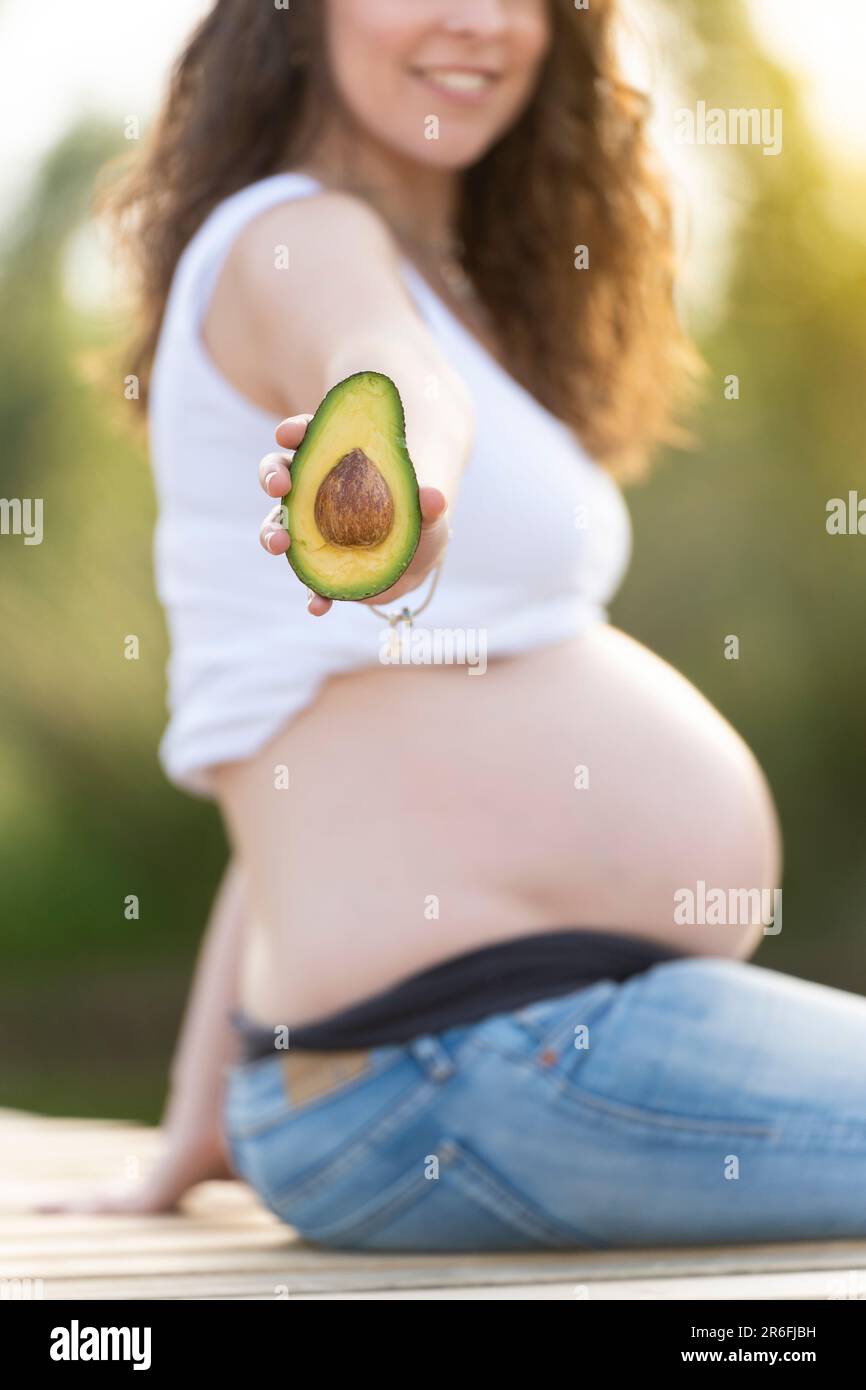 Pregnant woman holding an avocado and showing it to the camera Stock Photo