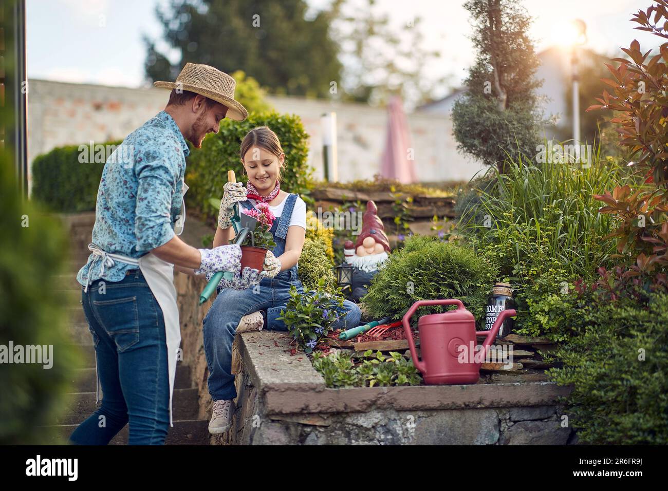 Father and young girl child assisting with re planting a flower from a flower pot, sitting by the flower garden by the house, feeling joyful. Home, fa Stock Photo