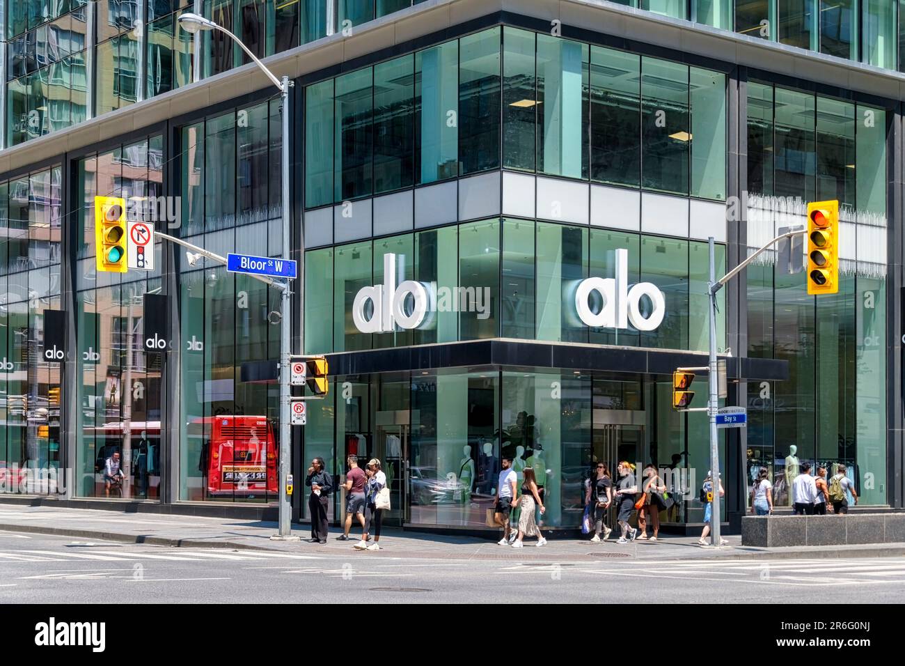 Toronto, Canada - June 4, 2023: Groups of people walking on a sidewalk alongside a building with a glass wall. The name 'Alo Alo' is prominently displ Stock Photo