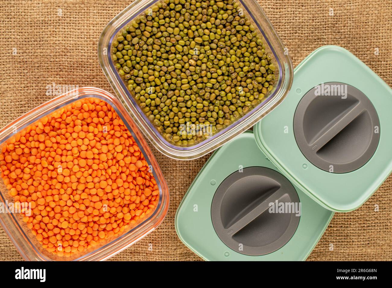 Red lentils and mung beans in plastic containers on jute cloth, macro