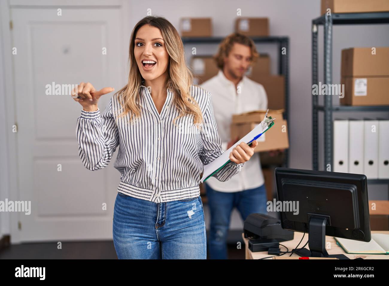 Blonde woman working at small business ecommerce pointing thumb up to ...