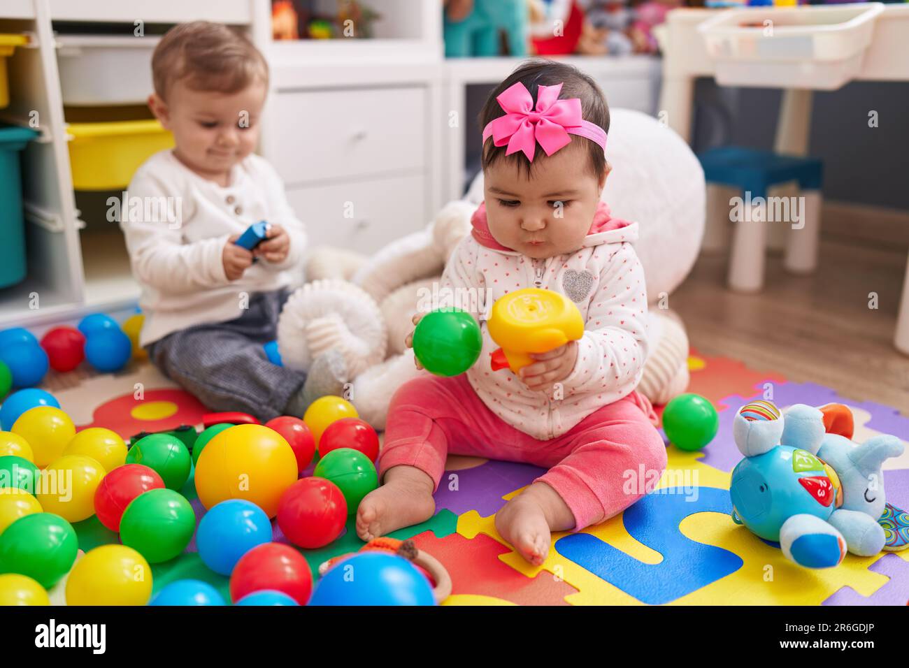 Adorable boy and girl playing with balls sitting on floor at kindergarten Stock Photo