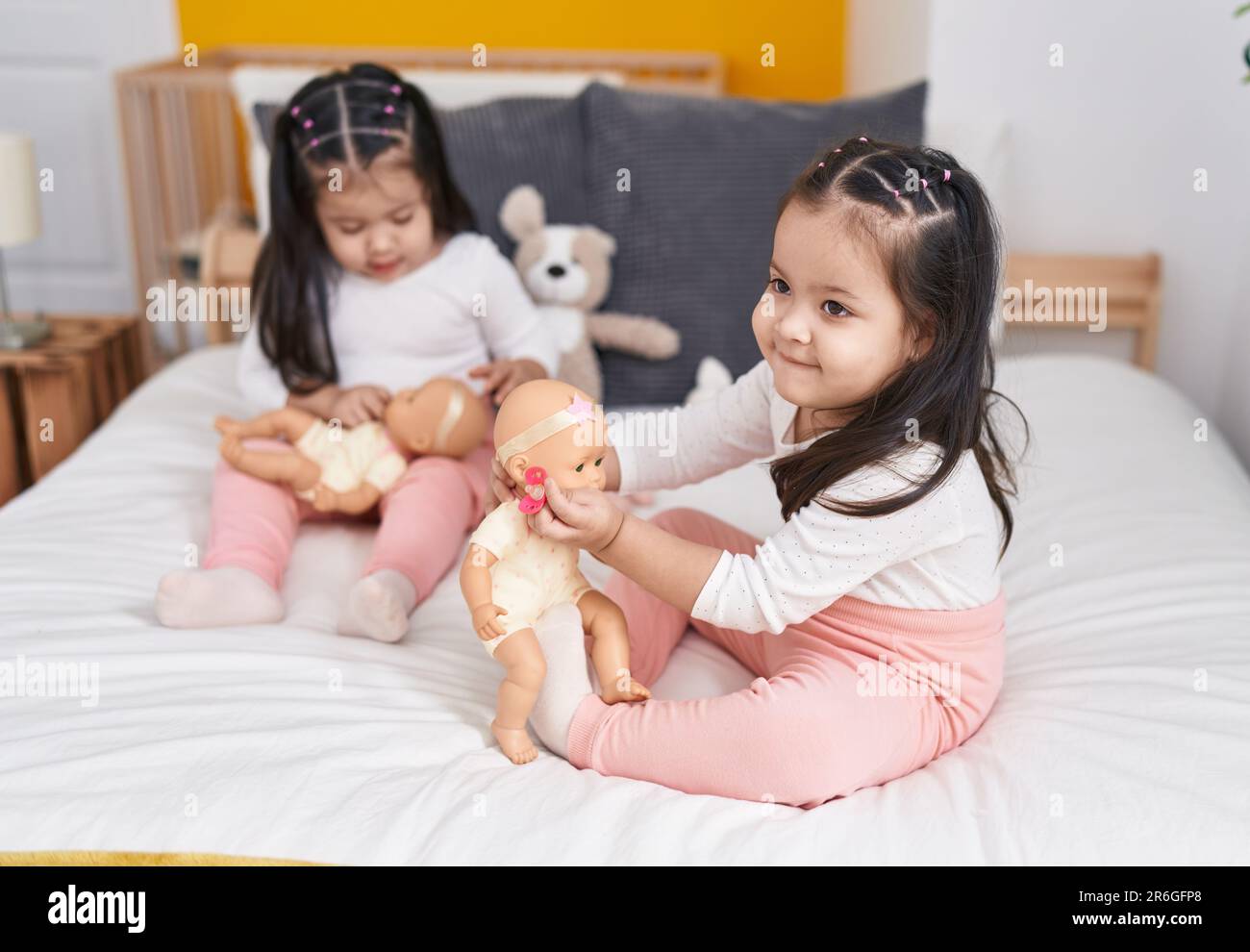 Adorable twin girls playing with baby doll sitting on bed at