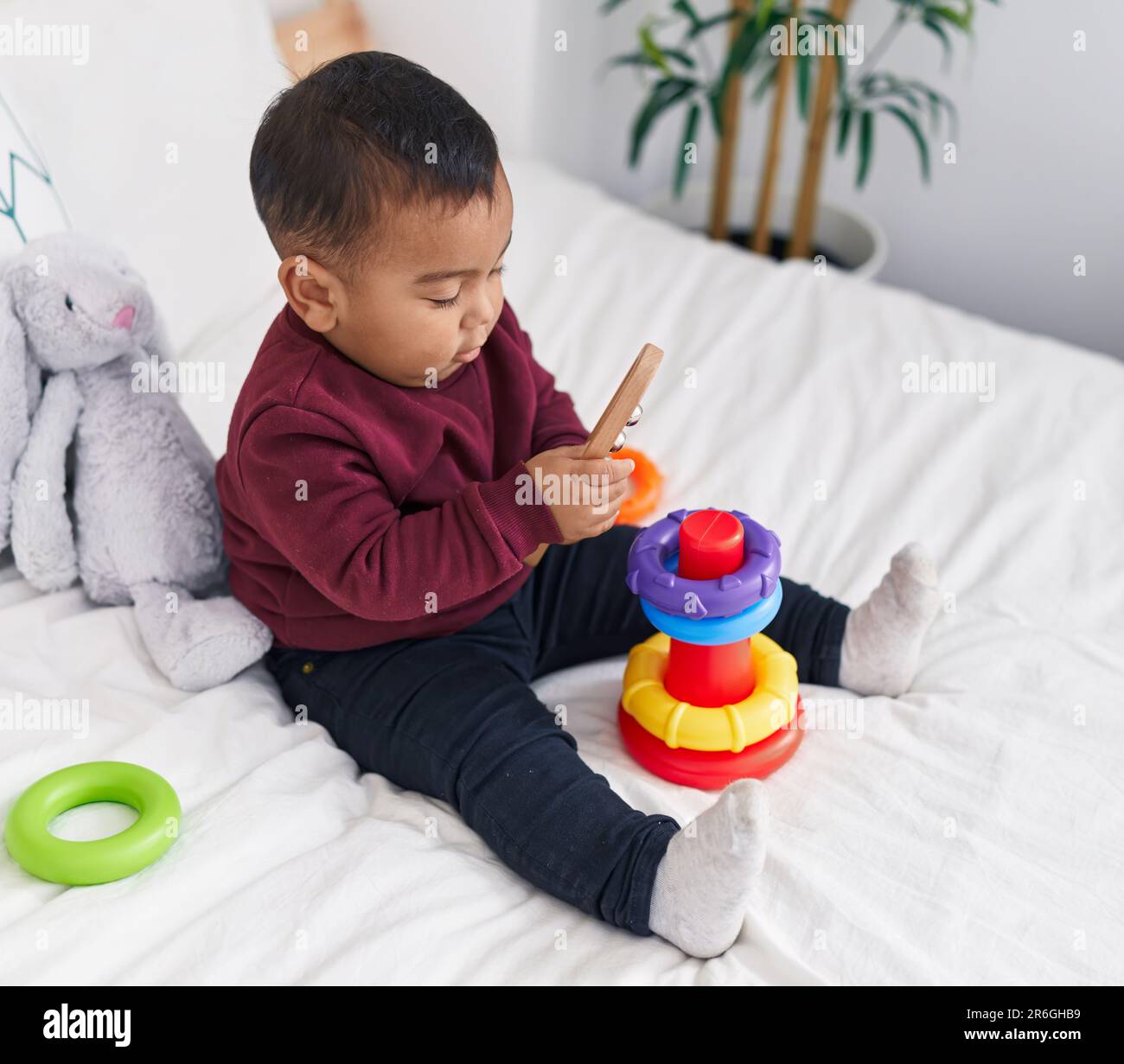 Adorable hispanic boy playing with hoops game sitting on bed at bedroom ...