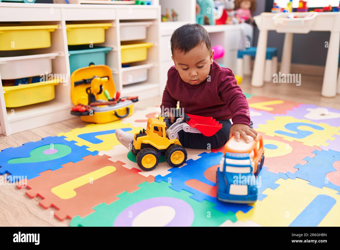 Adorable hispanic boy playing with car toy sitting on floor at ...
