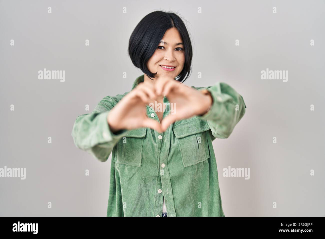 Young asian woman standing over white background smiling in love doing ...