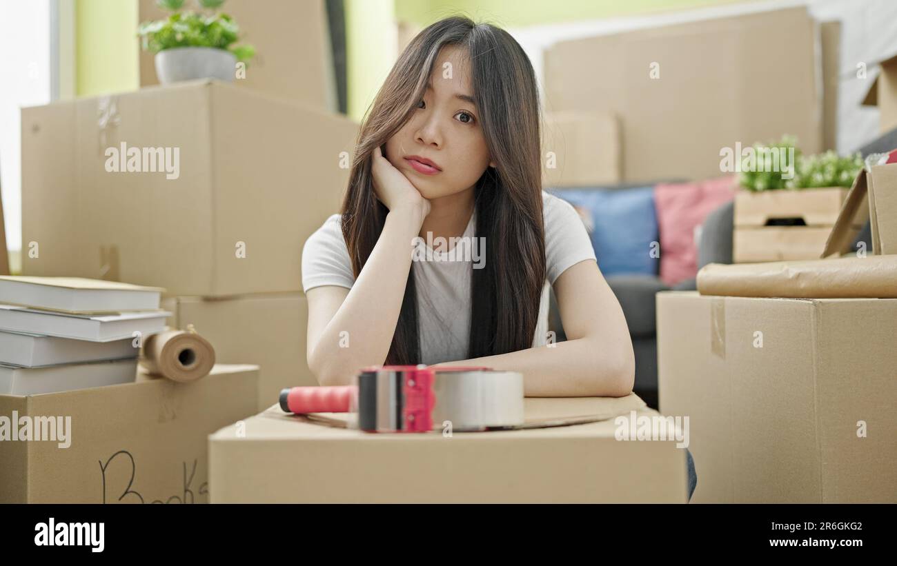 Young chinese woman sitting on floor with sad expression at new home ...