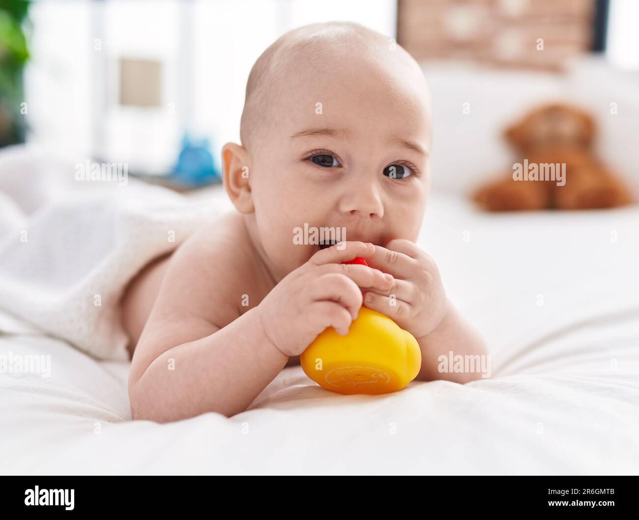Adorable caucasian baby lying on bed sucking duck toy at bedroom Stock ...