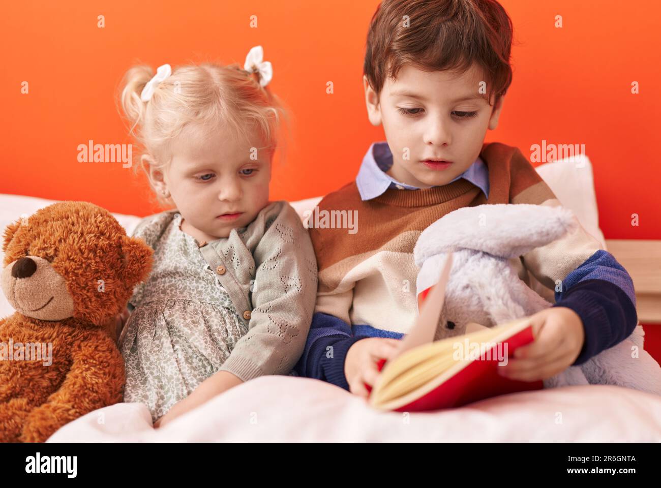 Adorable boy and girl reading book sitting on bed at bedroom Stock ...