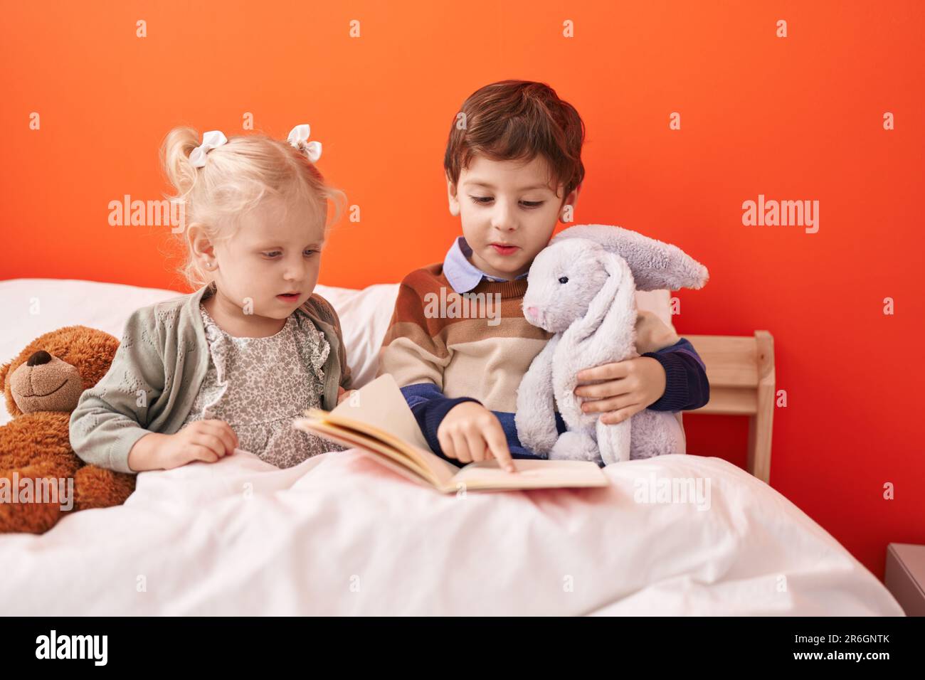 Adorable boy and girl reading book sitting on bed at bedroom Stock ...