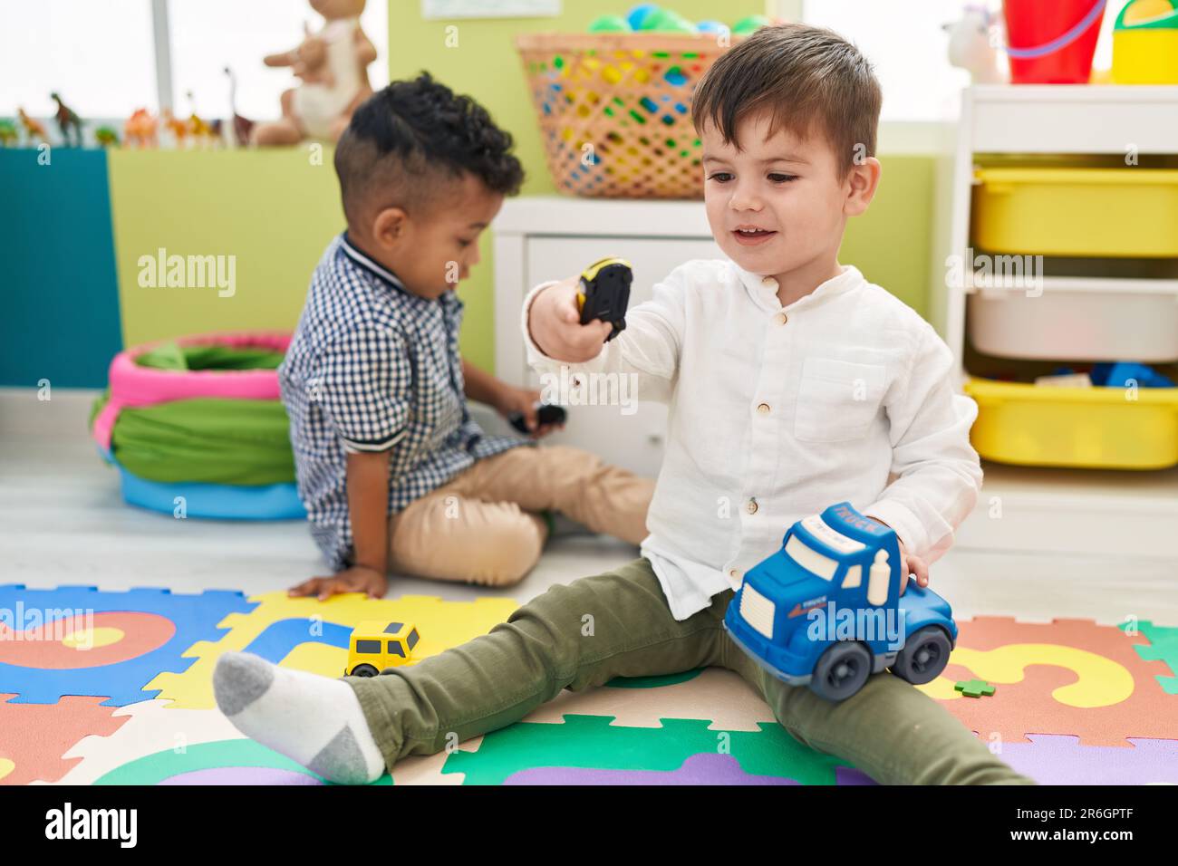 Adorable boys playing with cars toy sitting on floor at kindergarten ...