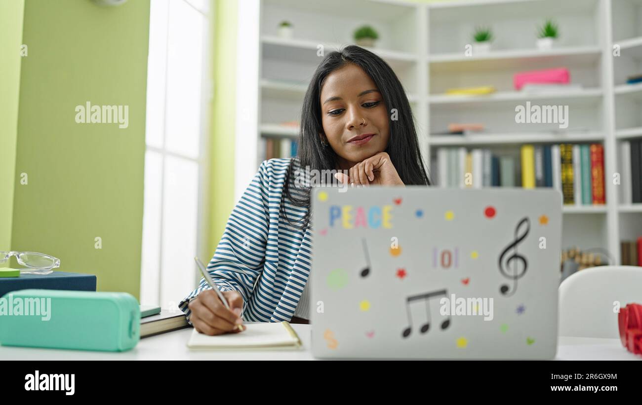 African american woman student using laptop writing notes at library ...