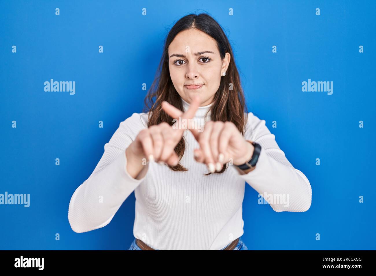 Young hispanic woman standing over blue background rejection expression ...