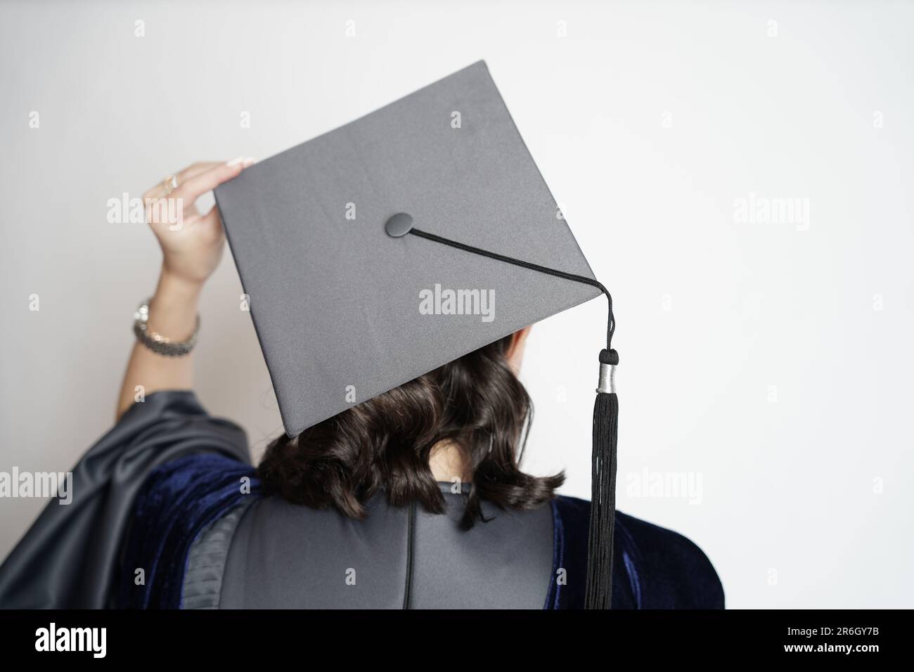 A clear photo of a girl wearing a graduation gown with white space for  text. A woman is standing on a white background wearing gown and cap. Stock Photo