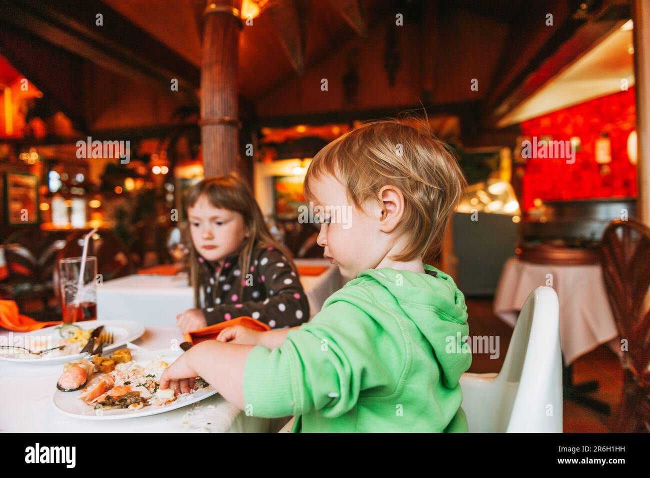 Two messy kids eating lunch in restaurant, toddler eating food with hands Stock Photo