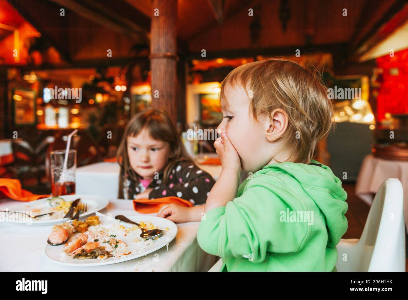Two messy kids eating lunch in restaurant, toddler eating food with hands Stock Photo