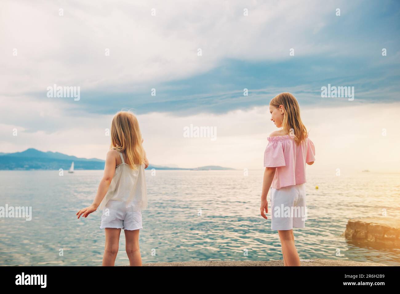 Little girls playing by the lake in summertime, children having fun outside, back view Stock Photo
