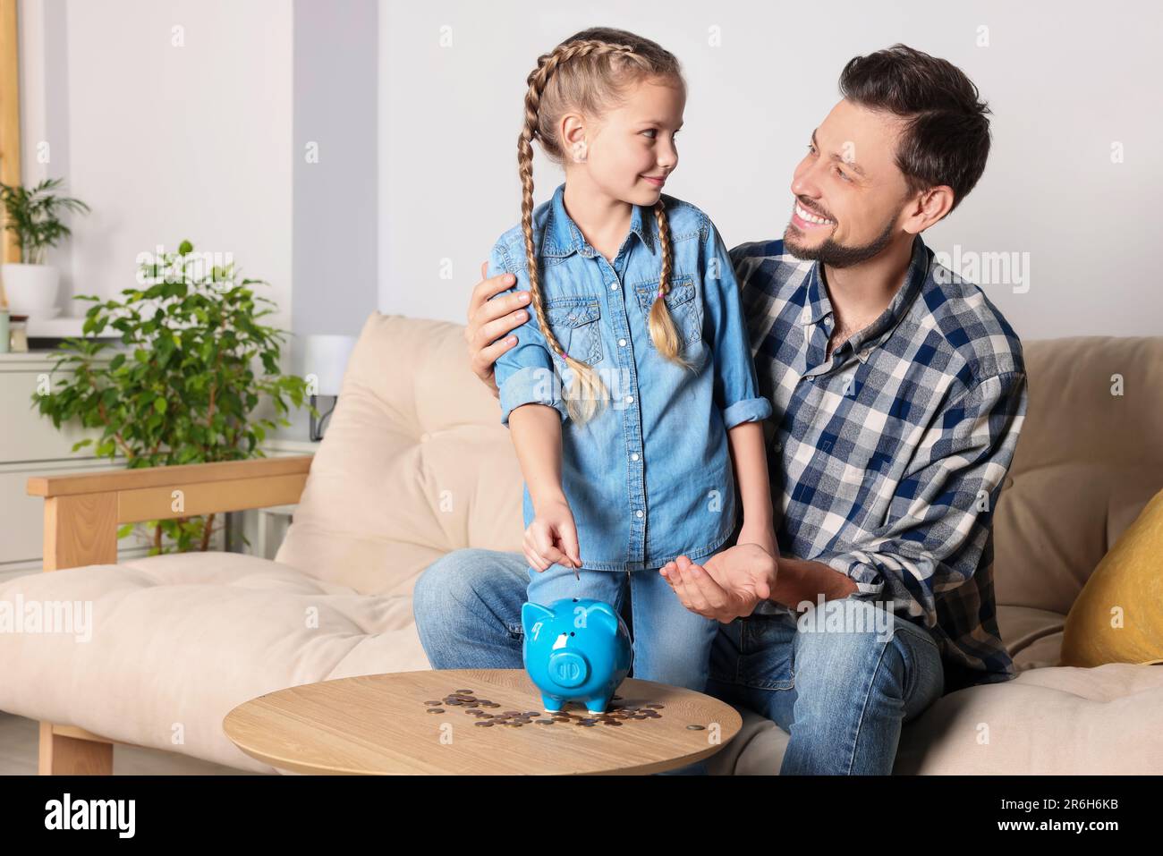 Little girl with her father putting coin into piggy bank at home Stock ...