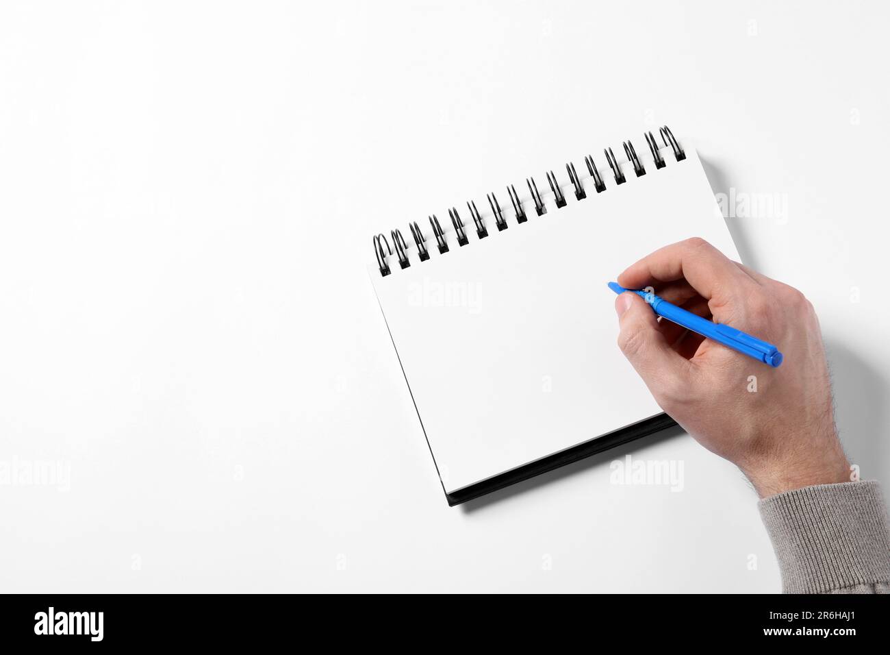 Man with pen and empty notepad on white background, top view. Space for ...