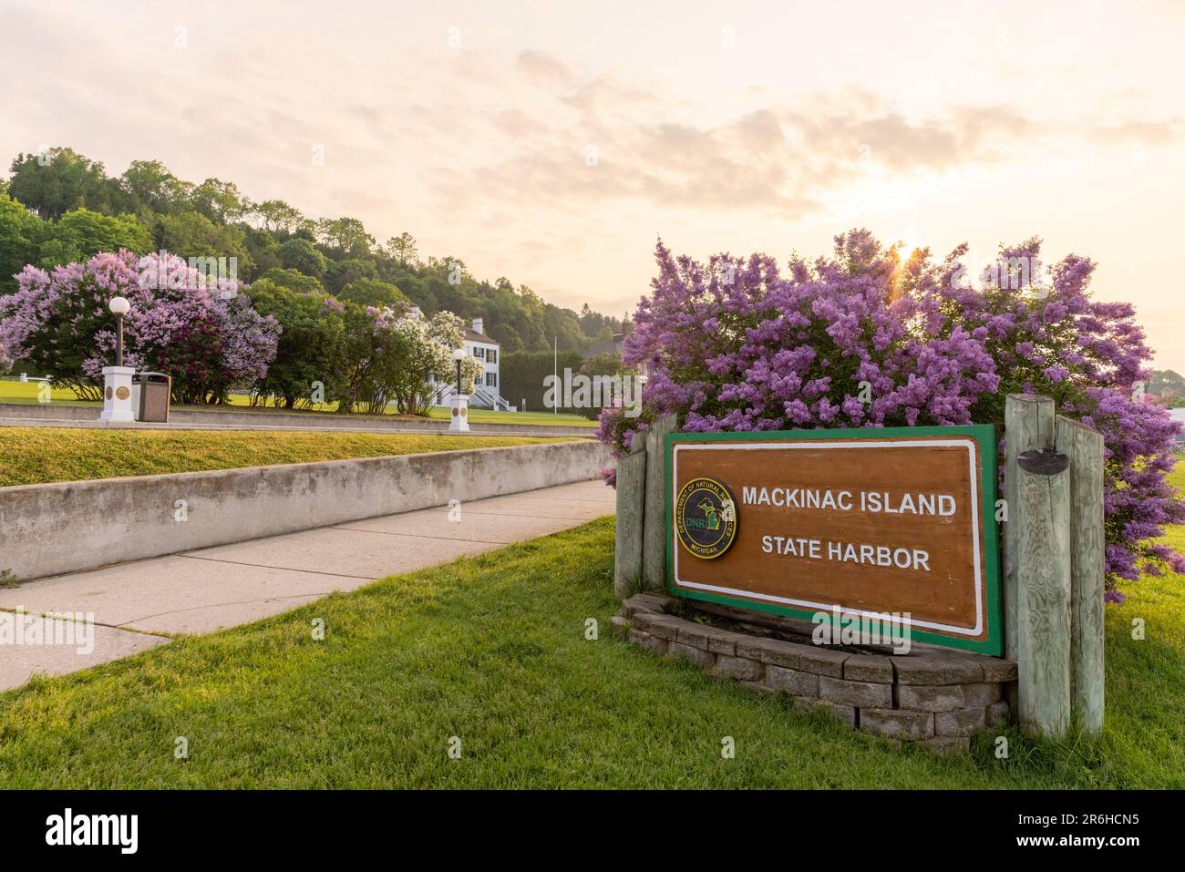 Purple lilacs and sunflare behind the sign for the Mackinac Island State Harbor sign during the lilac festival. Stock Photo