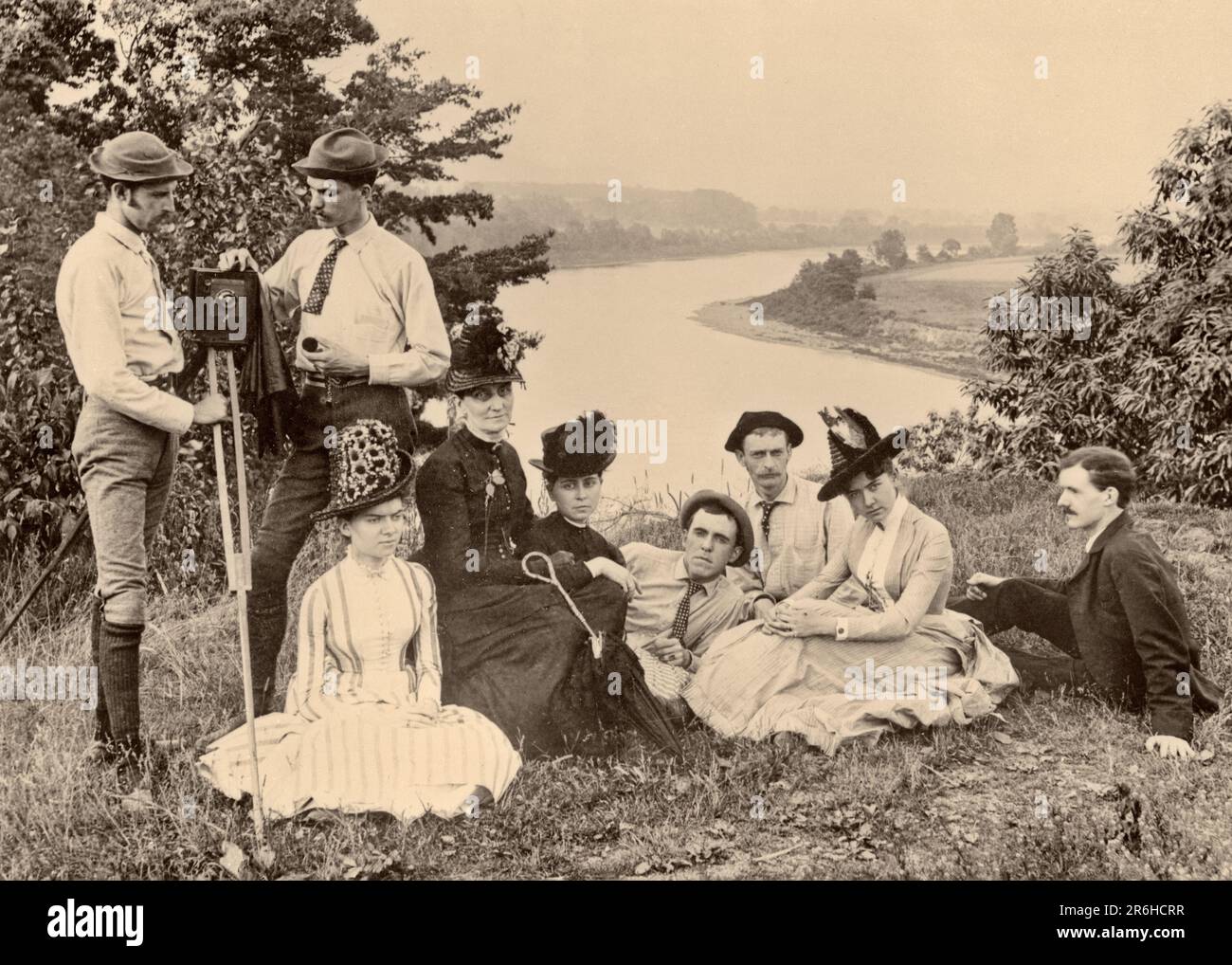 1890s FAMILY GROUP SITTING ON GROUND HILLTOP OVERLOOKING RIVER WHILE PHOTOGRAPHER & ASSISTANT PREPARE CAMERA FOR PICTURE - o2392 SPL001 HARS LADIES PERSONS THOUGHTFUL MALES MIDDLE-AGED 1800s B&W EYE CONTACT MIDDLE-AGED WOMAN HIGH ANGLE ADVENTURE LEISURE PREPARE EXCITEMENT RECREATION OCCUPATIONS ESCAPE FRIENDLY NINE STYLISH SINCERE SOLEMN 9 FOCUSED HILLTOP INTENSE MID-ADULT MID-ADULT MAN MID-ADULT WOMAN OVERLOOKING RELAXATION TOGETHERNESS YOUNG ADULT MAN YOUNG ADULT WOMAN & BLACK AND WHITE CAREFUL CAUCASIAN ETHNICITY EARNEST INTENT OLD FASHIONED Stock Photo