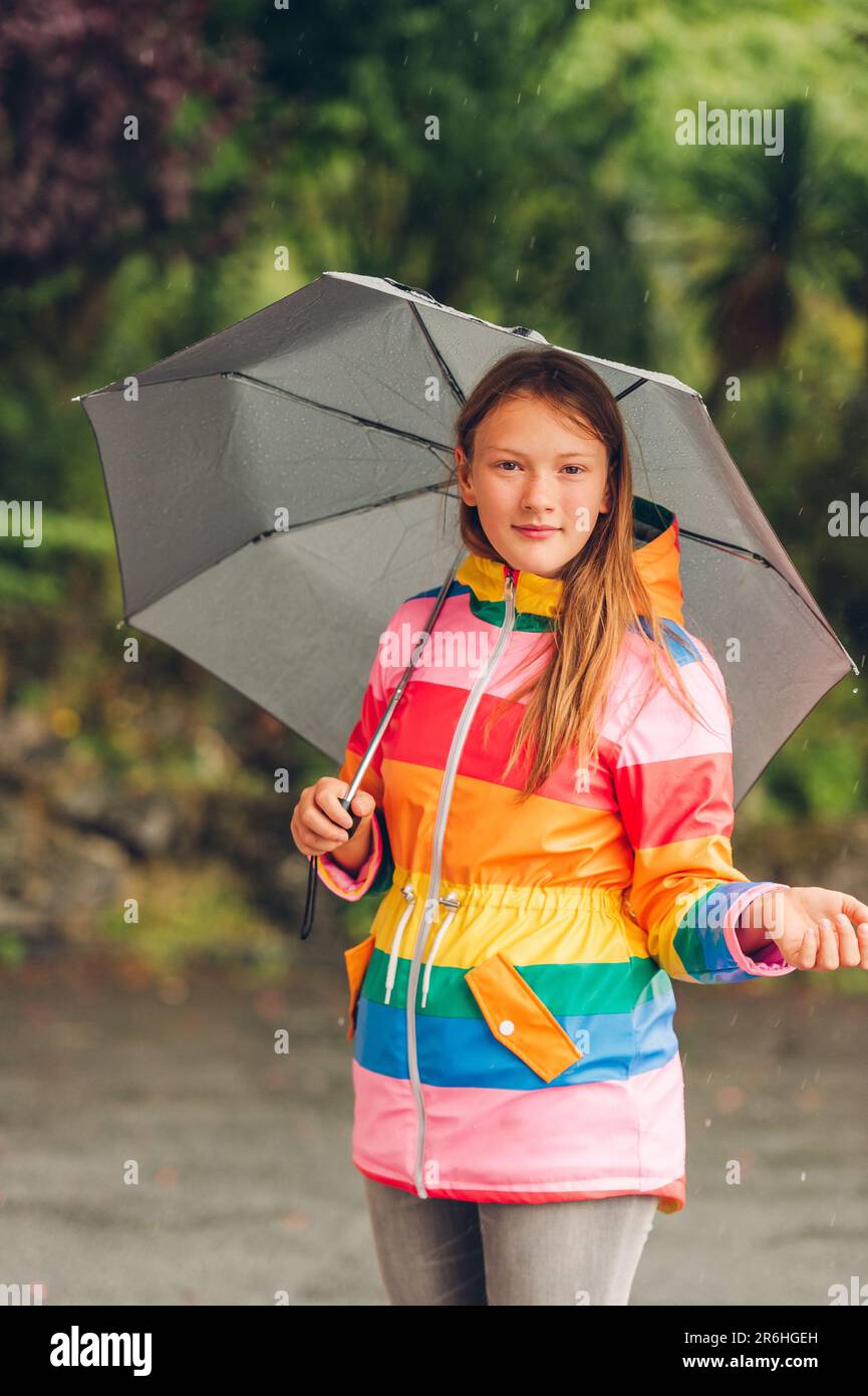 Outdoor portrait of young girl under the rain, holding umbrella, wearing colorful rain jacket Stock Photo