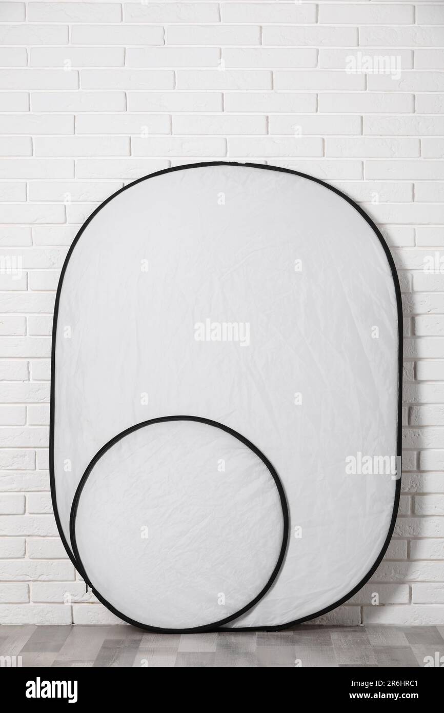 Professional light reflectors near white brick wall in room