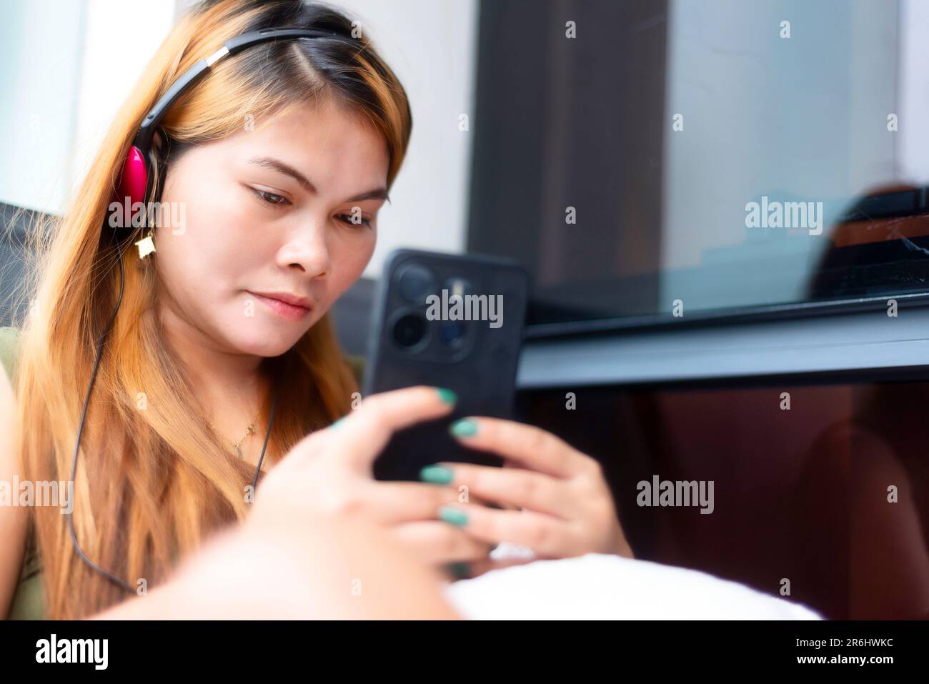 Sitting outside, on a high rise condo balcony,wearing headphones,speaking to her family who live in a remote part of rural Mindanao island,while she l Stock Photo