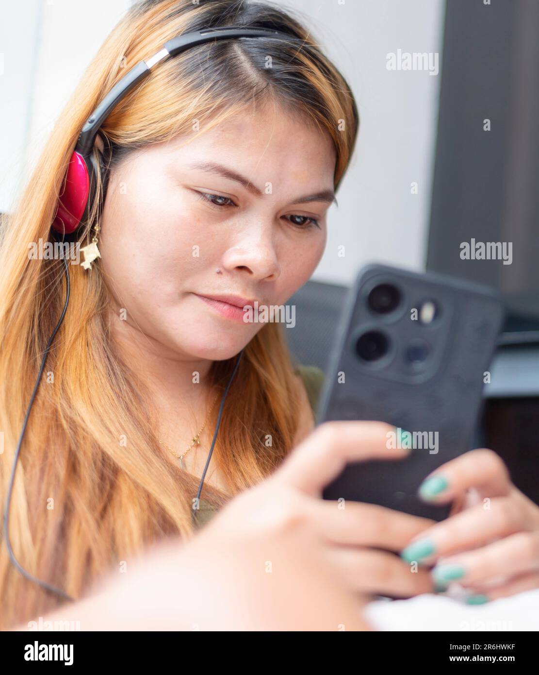 Sitting outside, on a high rise condo balcony,wearing headphones,speaking to her family who live in a remote part of rural Mindanao island,while she l Stock Photo