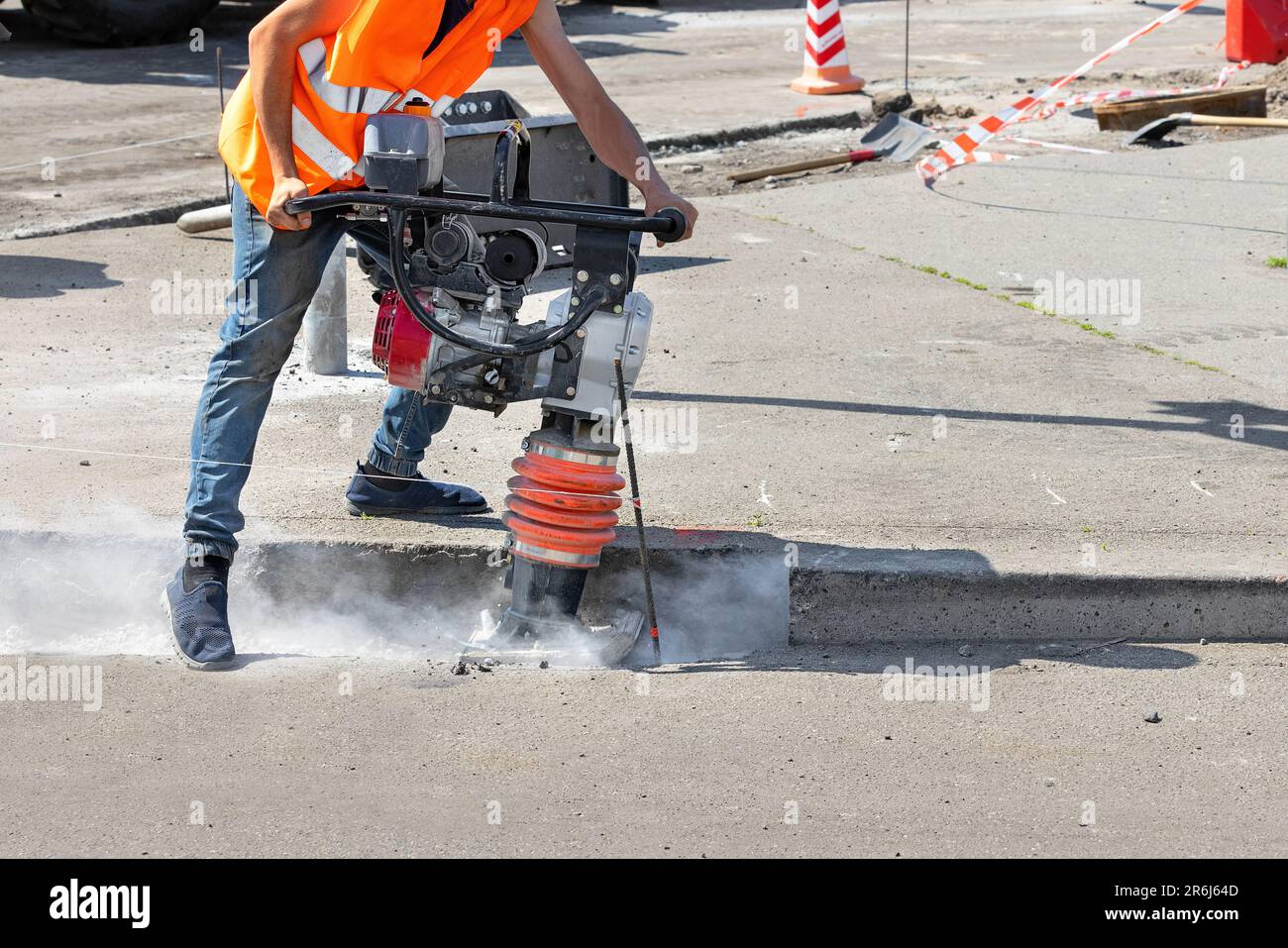 A construction worker is ramming a trench with a vibrating rammer at a construction site and kicking up a cloud of dust around him. Stock Photo