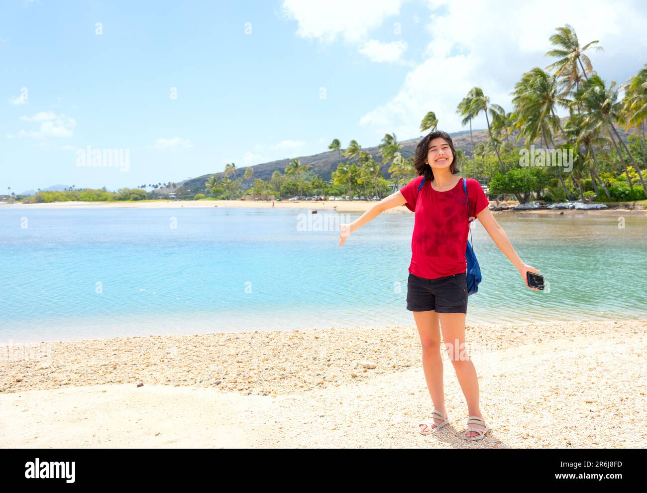 Young woman standing on quiet beach by a calm bay in  Oahu, Hawaii Stock Photo