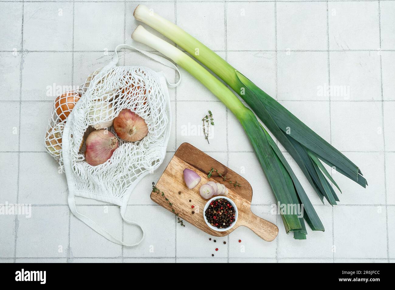 Wooden board and string bag with different kinds of onion on white tile ...