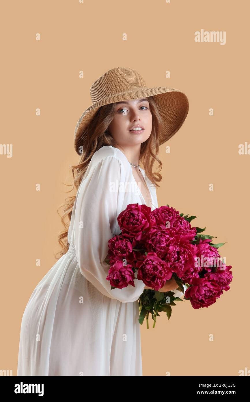 Beautiful young woman with bouquet of peony flowers on beige background ...