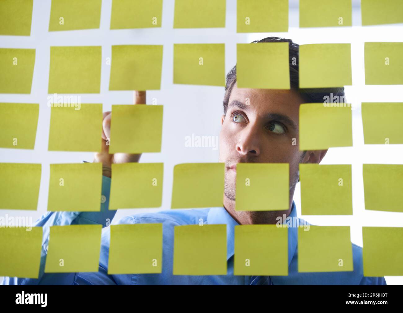 Creative man, face and thinking, pointing to sticky note in schedule brainstorming or planning tasks on glass board. Thoughtful male contemplating Stock Photo