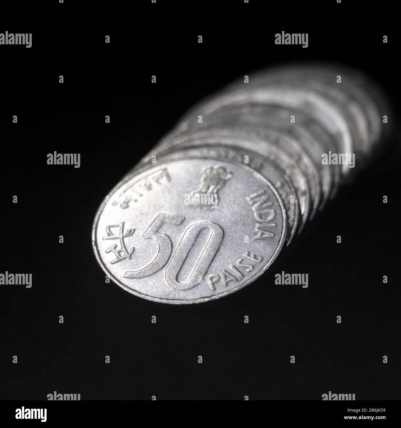 shiny vintage silver fifty or 50 paisa coins of india stacked together back to back in a row isolated in a black background in closeup Stock Photo