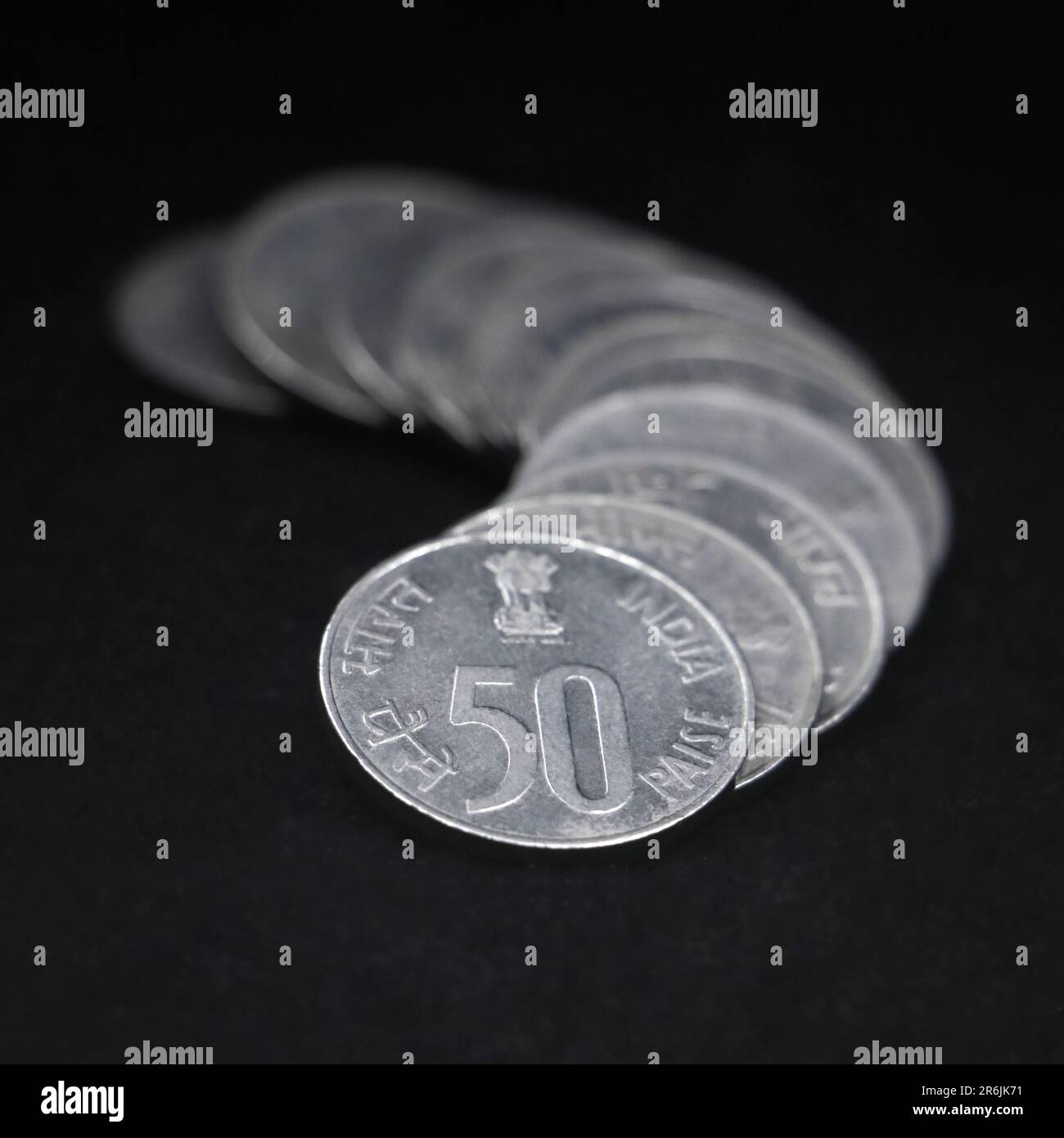 shiny vintage silver fifty or 50 paisa coins of india stacked together back to back in a row isolated in a black background in closeup Stock Photo