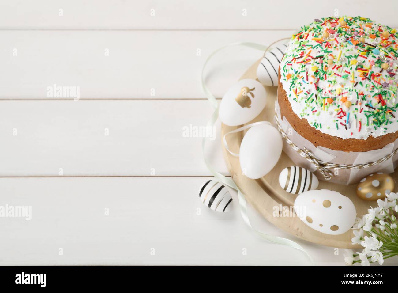 Traditional Easter cake with sprinkles and painted eggs on white wooden ...