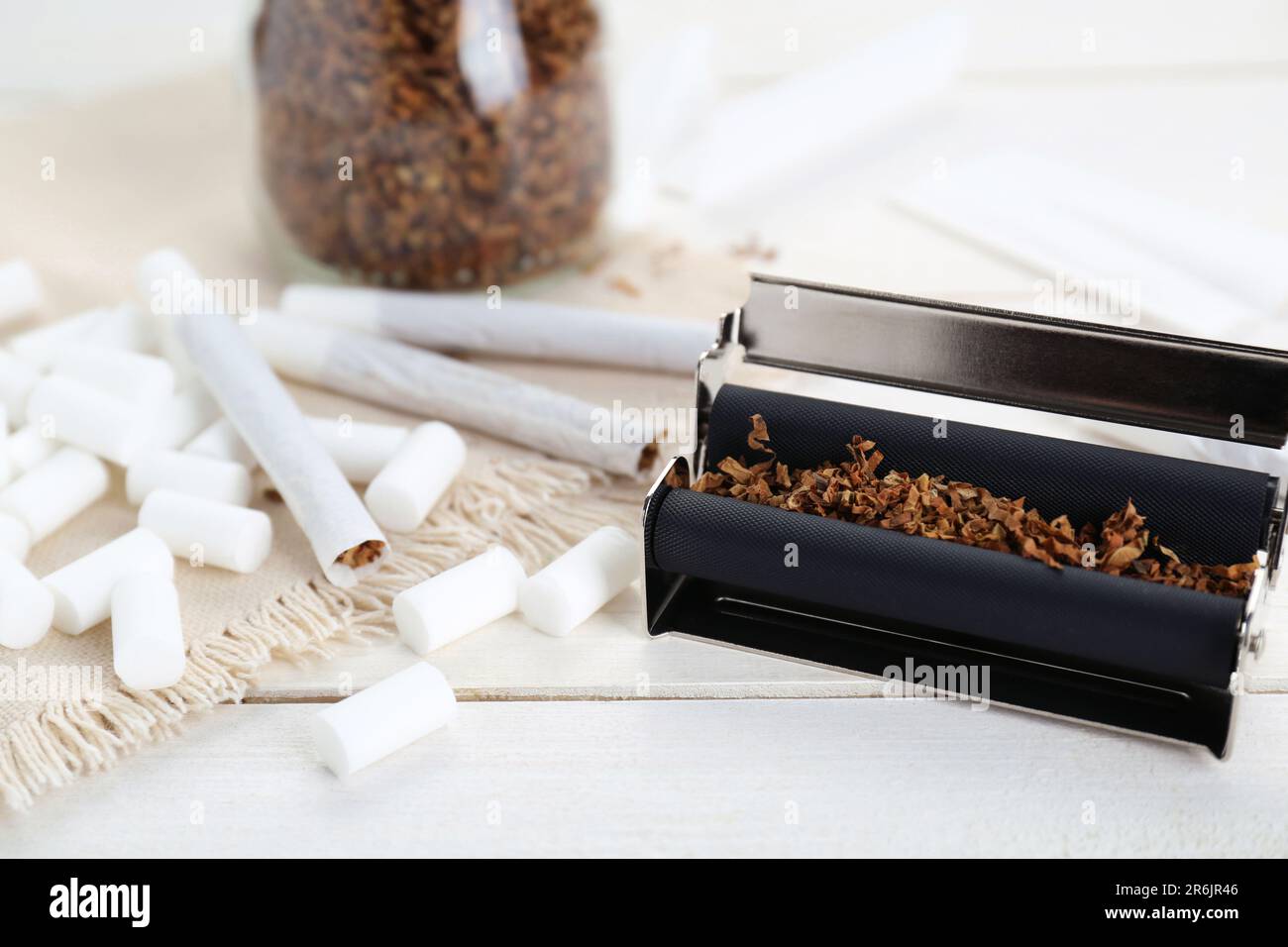 Hand rolled cigarettes, filters and tobacco on white wooden table, closeup  Stock Photo