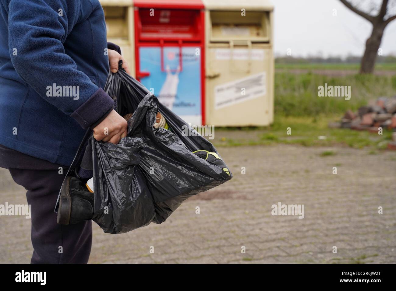 Women's hands with a bag of old shoes on the background of garbage cans