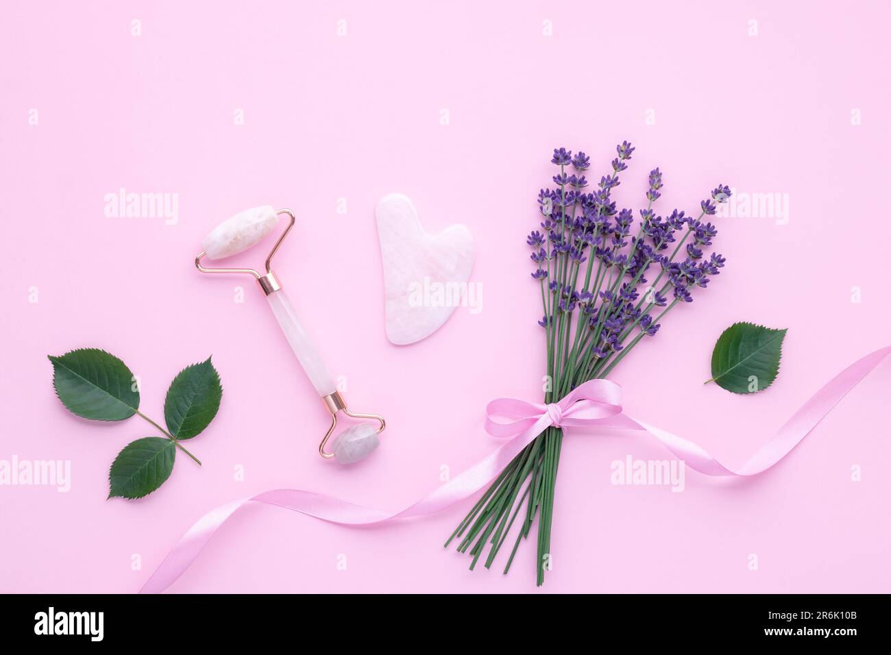 Quartz face roller on pink background, top view. Facial massage tool. Skin care, treatment concept. Gua sha massager made from natural jade and rose s Stock Photo