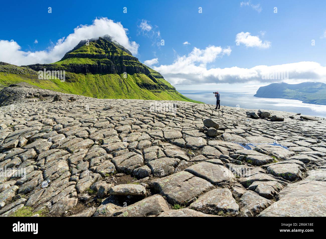 One tourist photographing Skaelingsfjall mountain standing on cracked soil in summer, Streymoy Island, Faroe Islands, Denmark, Europe Stock Photo