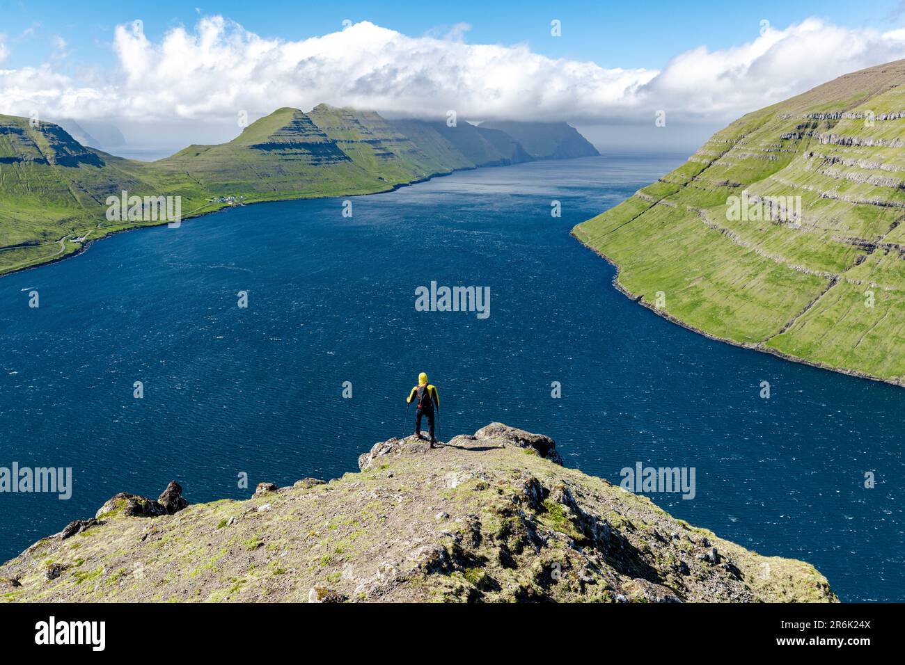 High angle view of hiker admiring mountains and ocean standing on top of a mountain, Klaksvik, Bordoy Island, Faroe Islands, Denmark, Europe Stock Photo