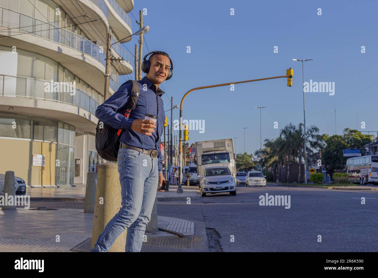 Young latin man with headphones and casual clothing crossing the street in a city with copy space. Stock Photo