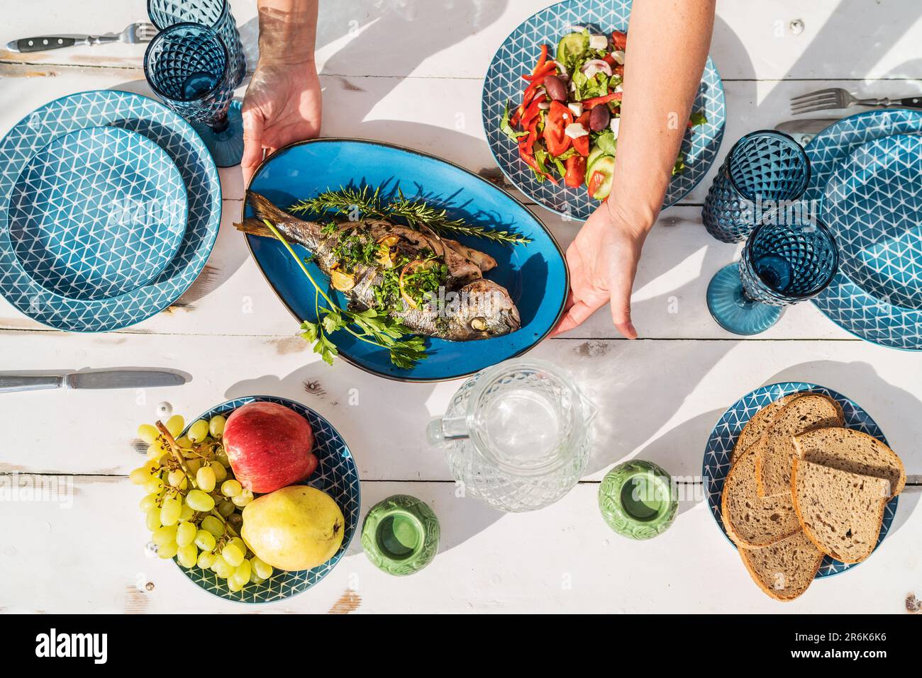 Gilt-head bream also known as Orata grilled on a barbeque grill served by a woman on a white wooden table with vegetable salad and fruits. Healthy sea Stock Photo