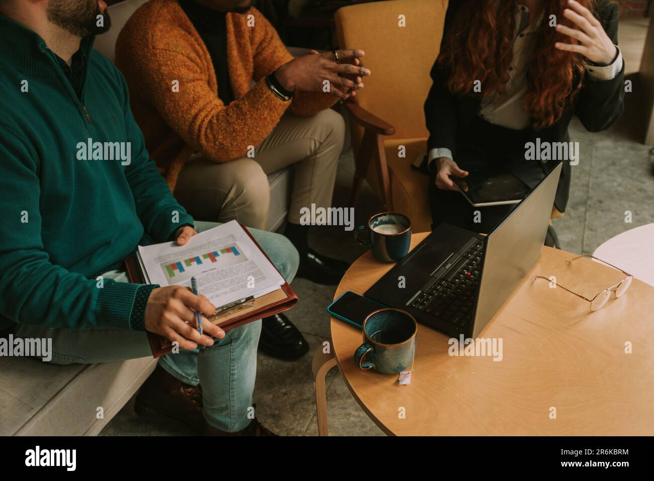 Three multiracial colleagues discussing statistics and teamwork results while having coffee time at the coffee bar Stock Photo